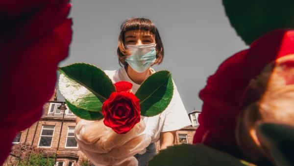 girl in mask proffering red rose to camera 